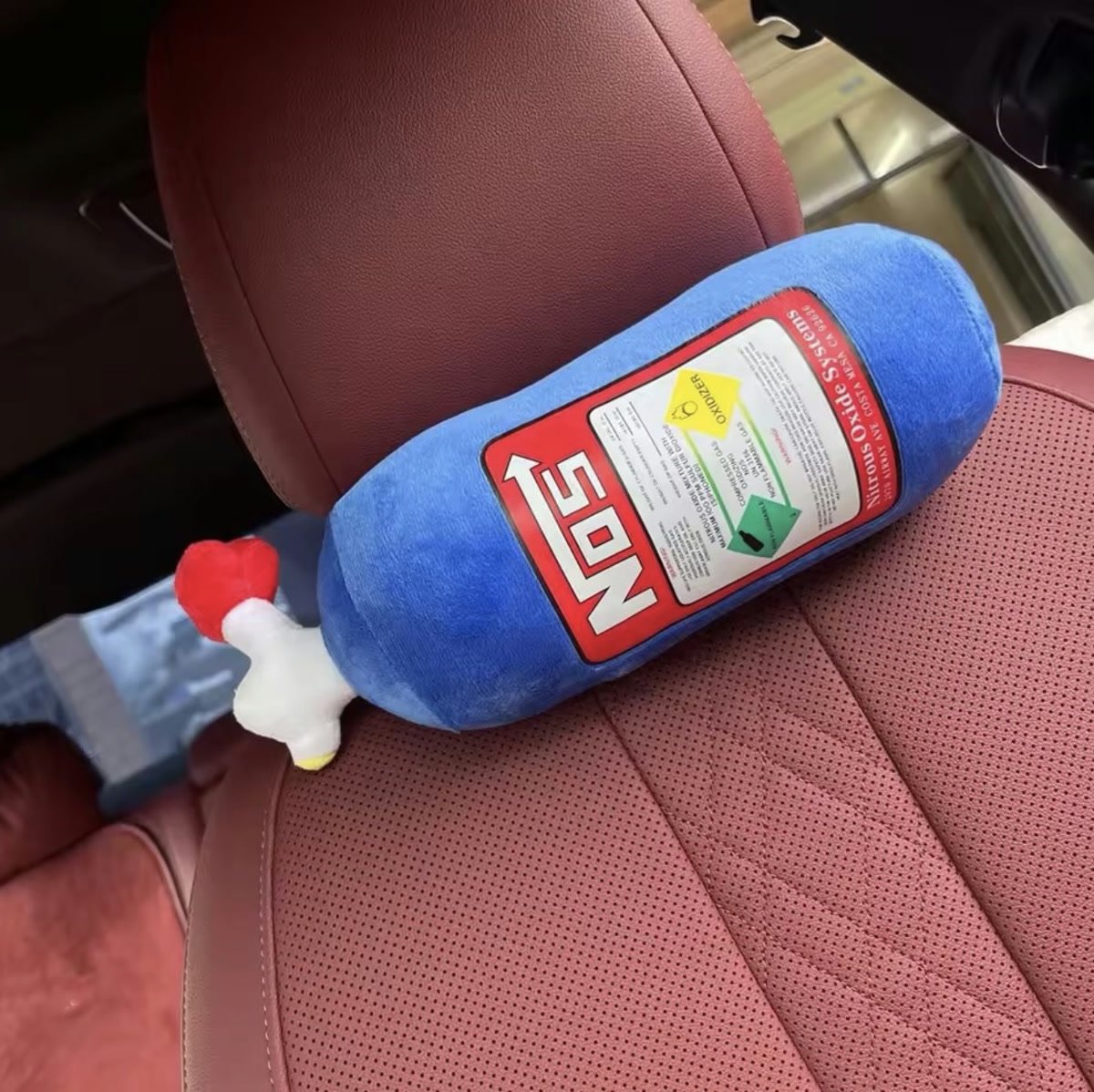 A blue nitrous bottle plush cushion resting against a car headrest